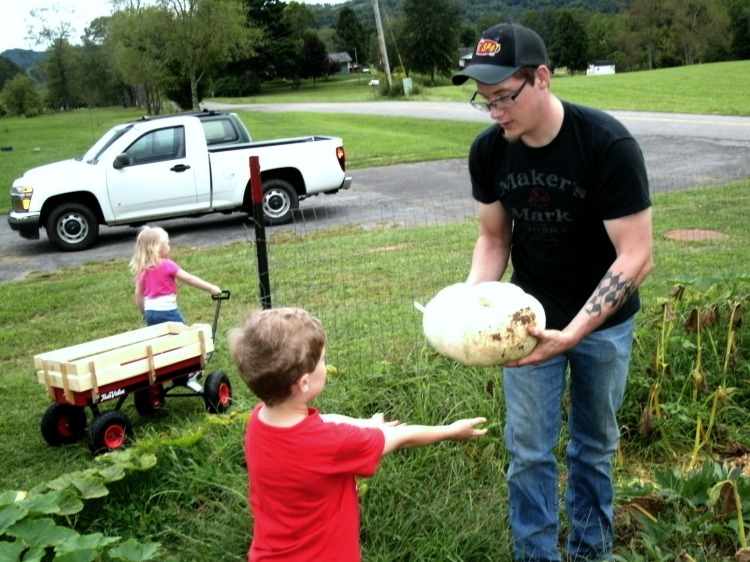 Cody hands Christopher a pumpkin as Paige brings the wagon around  to fill it